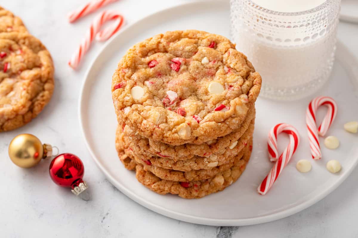 Stack of white chocolate peppermint cookies on a white plate next to a glass of milk.