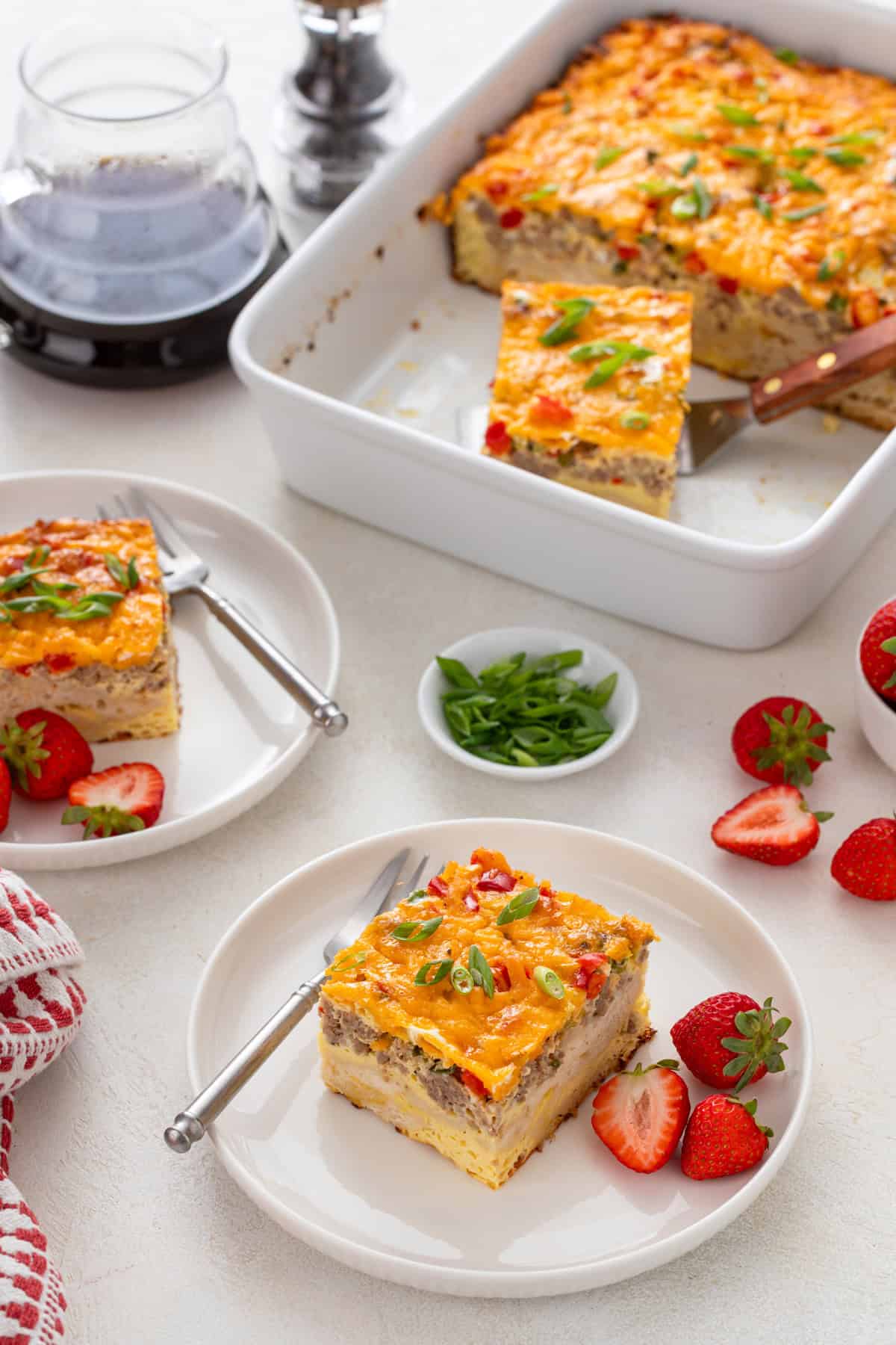 White plates holding slices of christmas breakfast casserole and fresh strawberries.