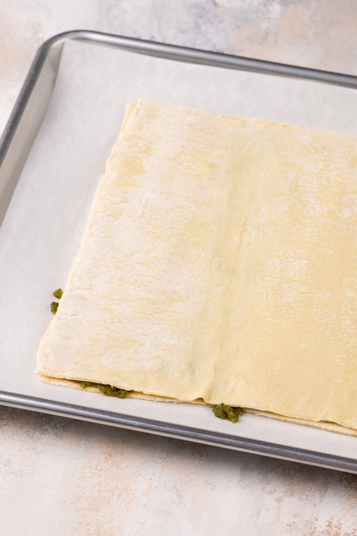 Two sheets of puff pastry sandwiching basil pesto on a sheet tray.