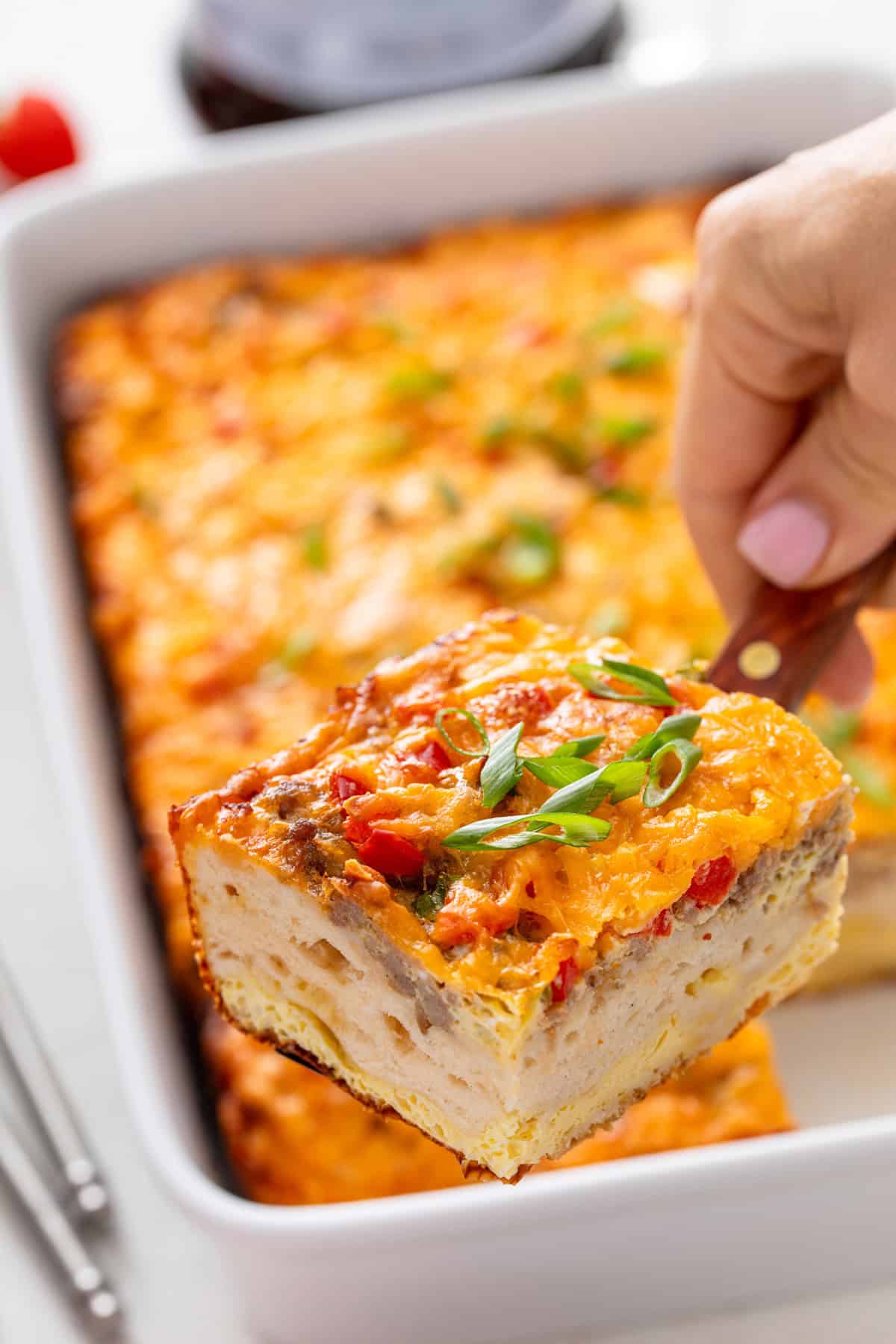 Hand using a spatula to lift up a slice of christmas breakfast casserole.