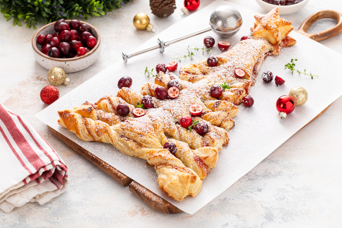 Puff pastry christmas tree filled with cranberry sauce on a piece of parchment paper on a wooden board.