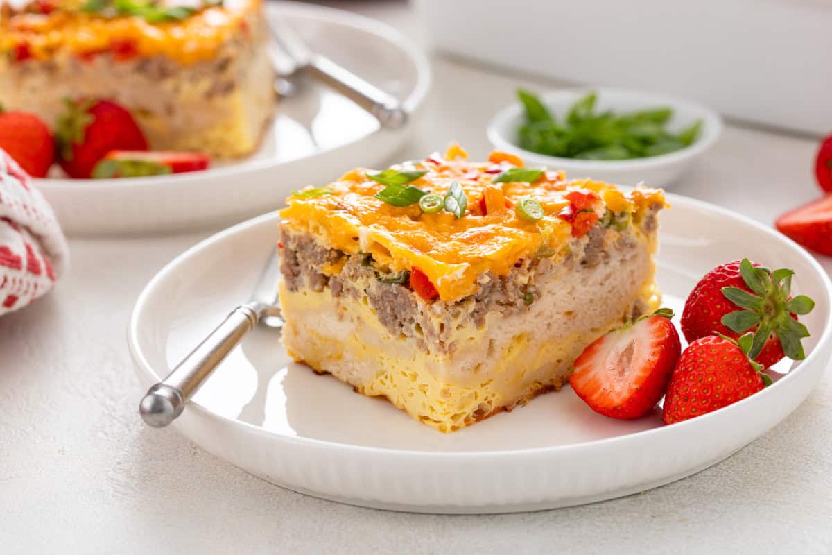 White plate holding a slice of christmas breakfast casserole and fresh strawberries.