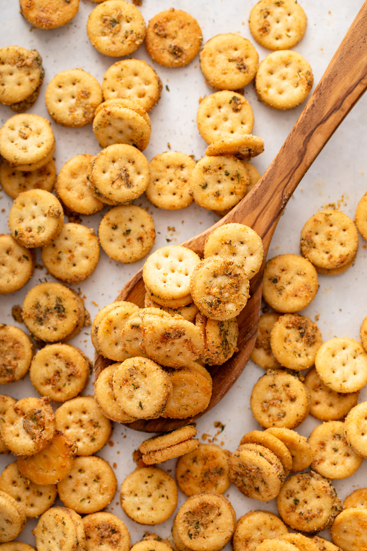 Wooden spoon about to lift a scoopful of ranch crackers off a baking sheet.