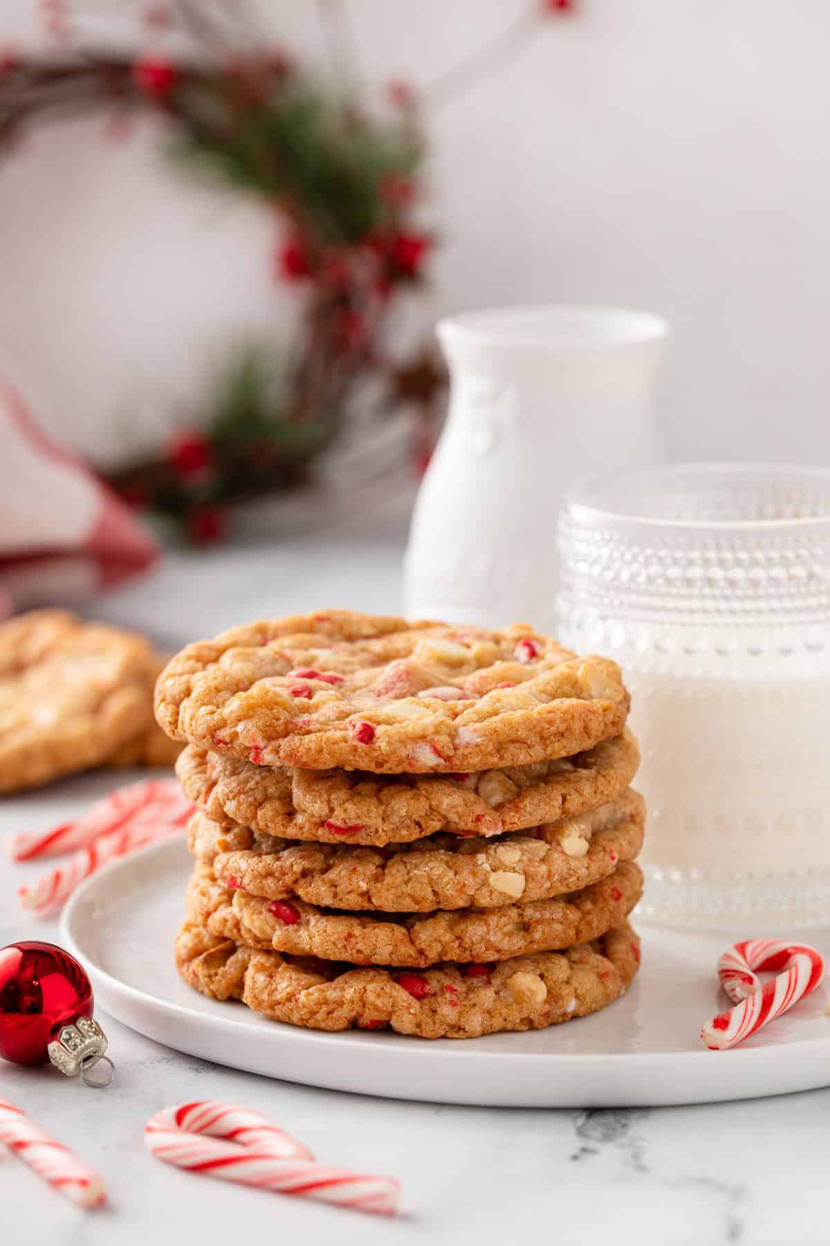 Side view of 5 stacked white chocolate peppermint cookies in front of a glass of milk on a white plate.