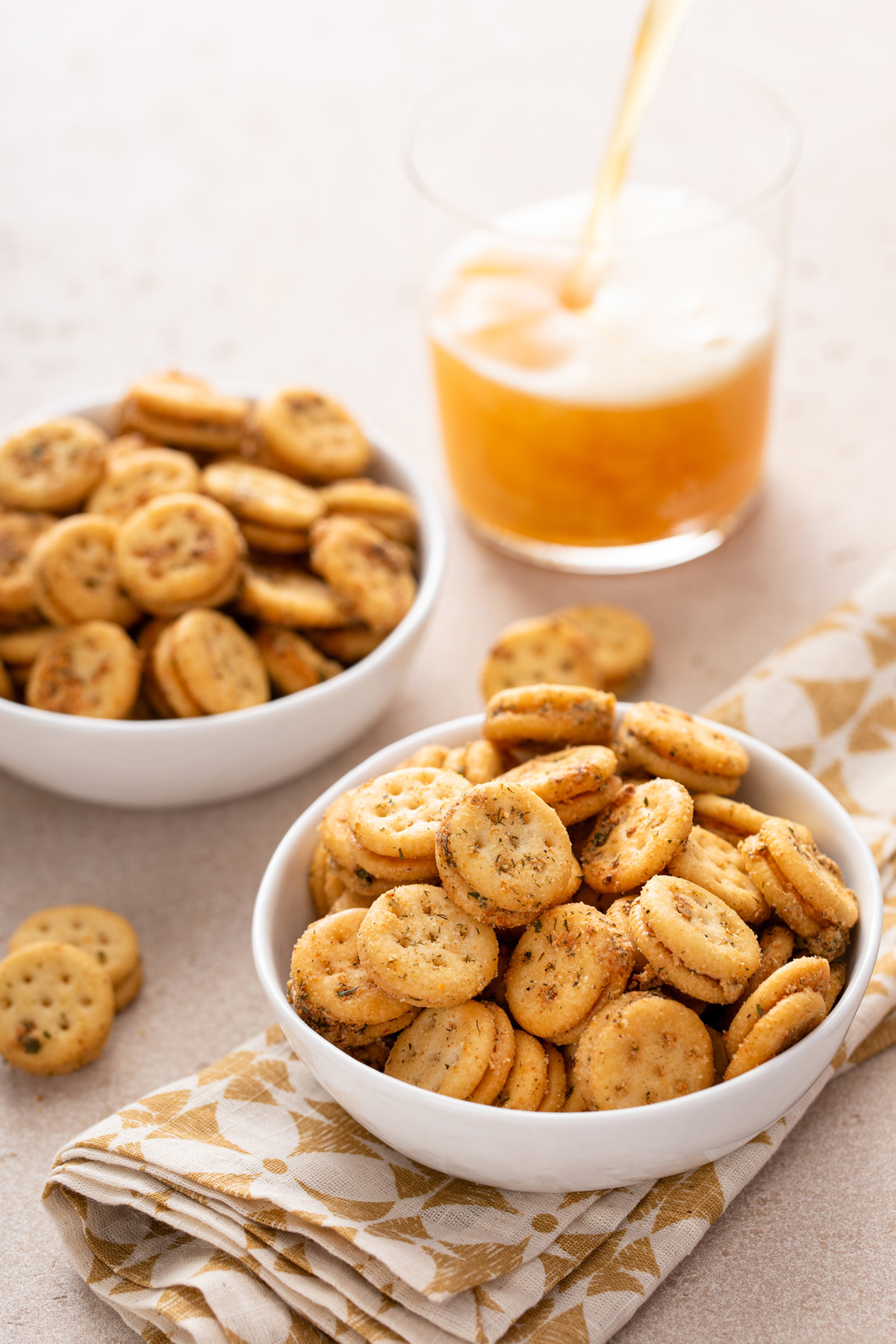 Two white bowls filled with ranch crackers with a beer being poured in the background.