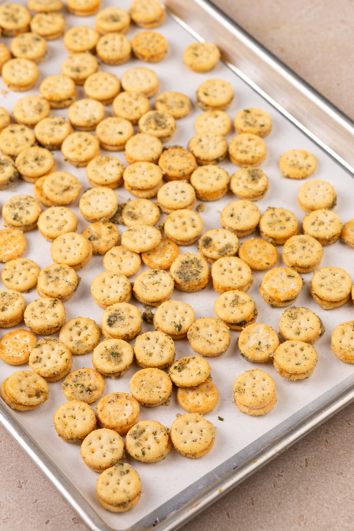 Unbaked ranch crackers spread on a lined baking sheet.