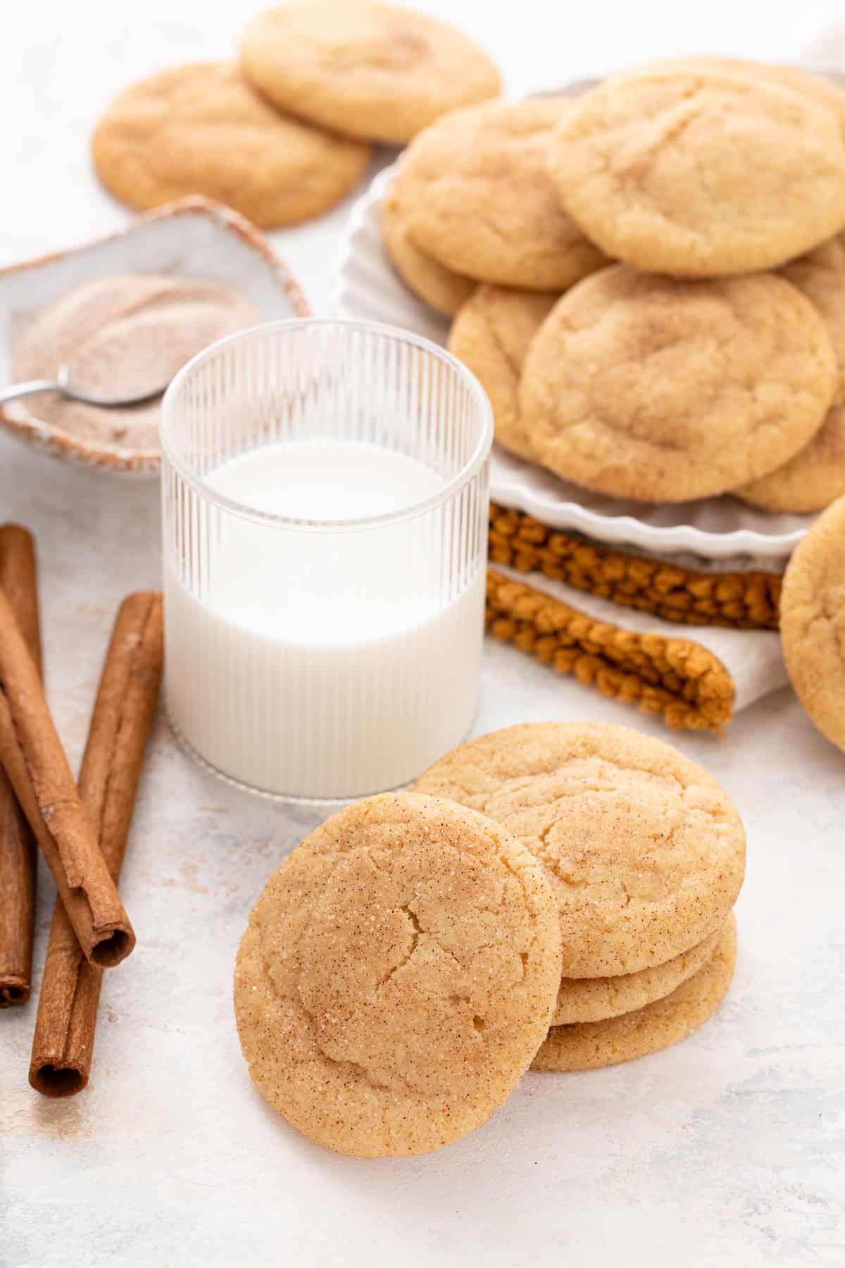 Four brown butter snickerdoodles stacked in front of a glass of milk.