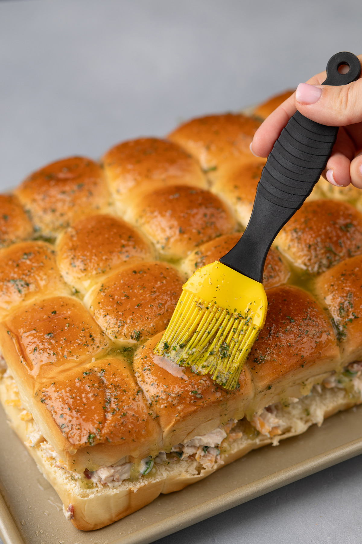 Garlic butter being brushed over the tops of chicken bacon ranch sliders.