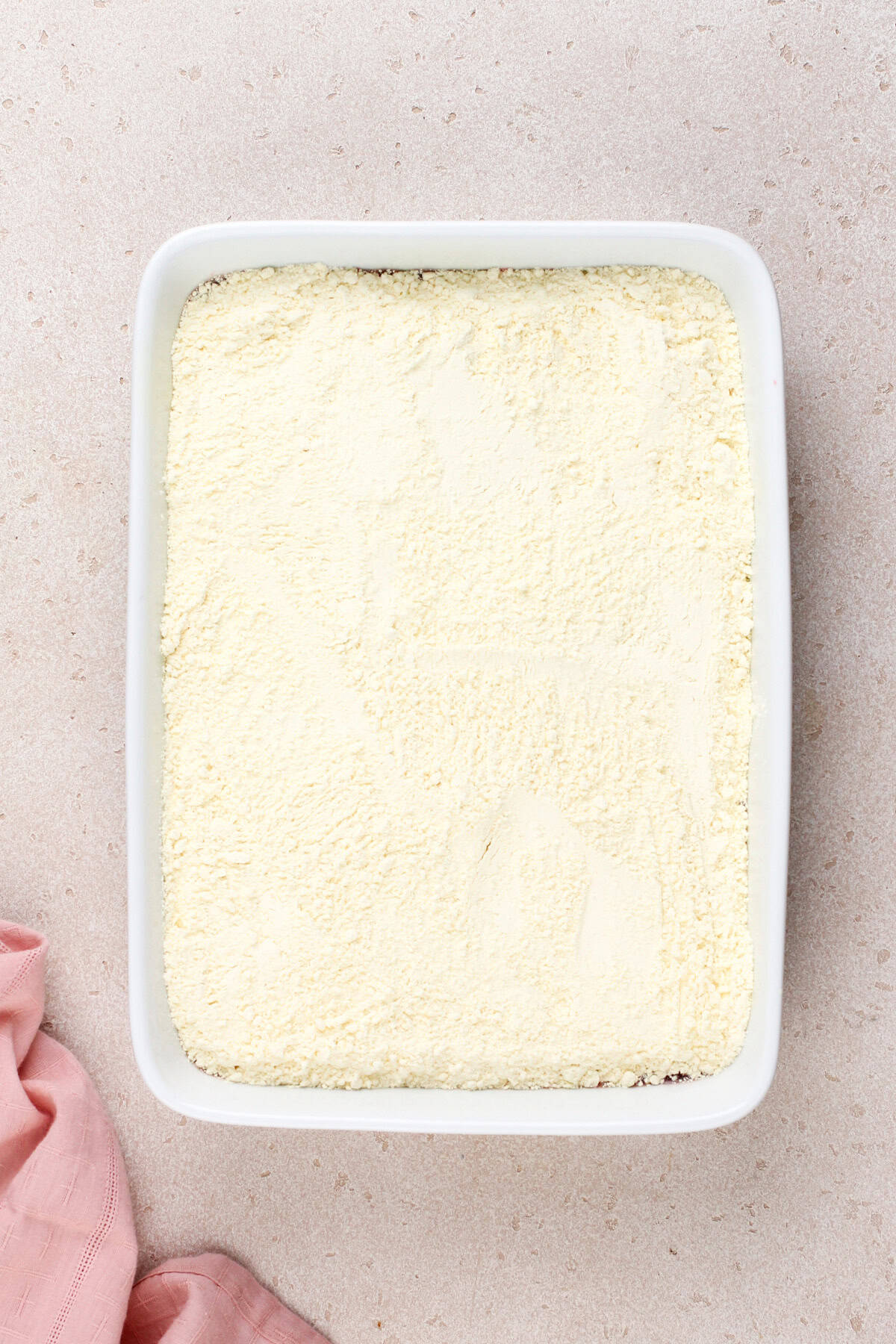 Cake mix sprinkled over cherry pie filling in a white baking dish.