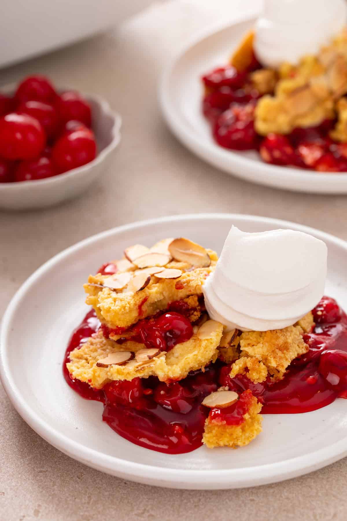 Serving of cherry dump cake on a white plate topped with whipped cream.