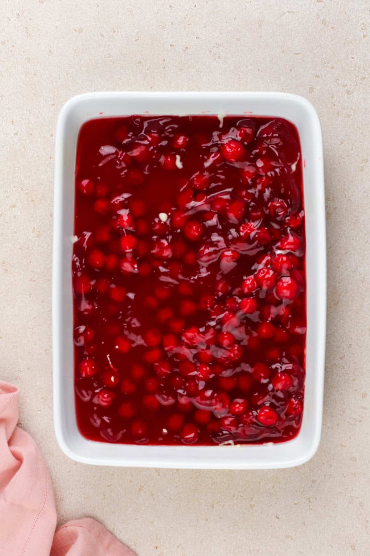 Cherry dump cake filling ingredients in a white baking dish.