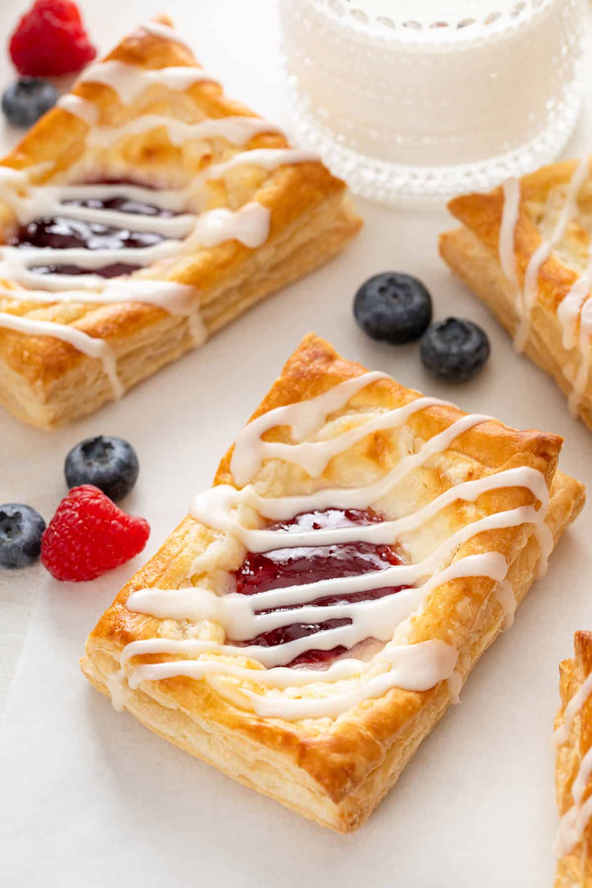 Close up of a puff pastry danish on a white countertop next to mixed berries.