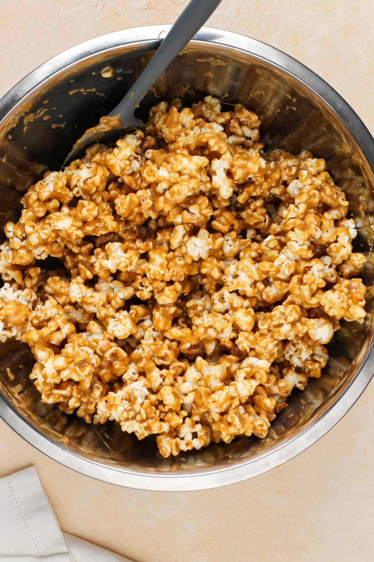 Caramel sauce and popcorn being stirred together in a large bowl.