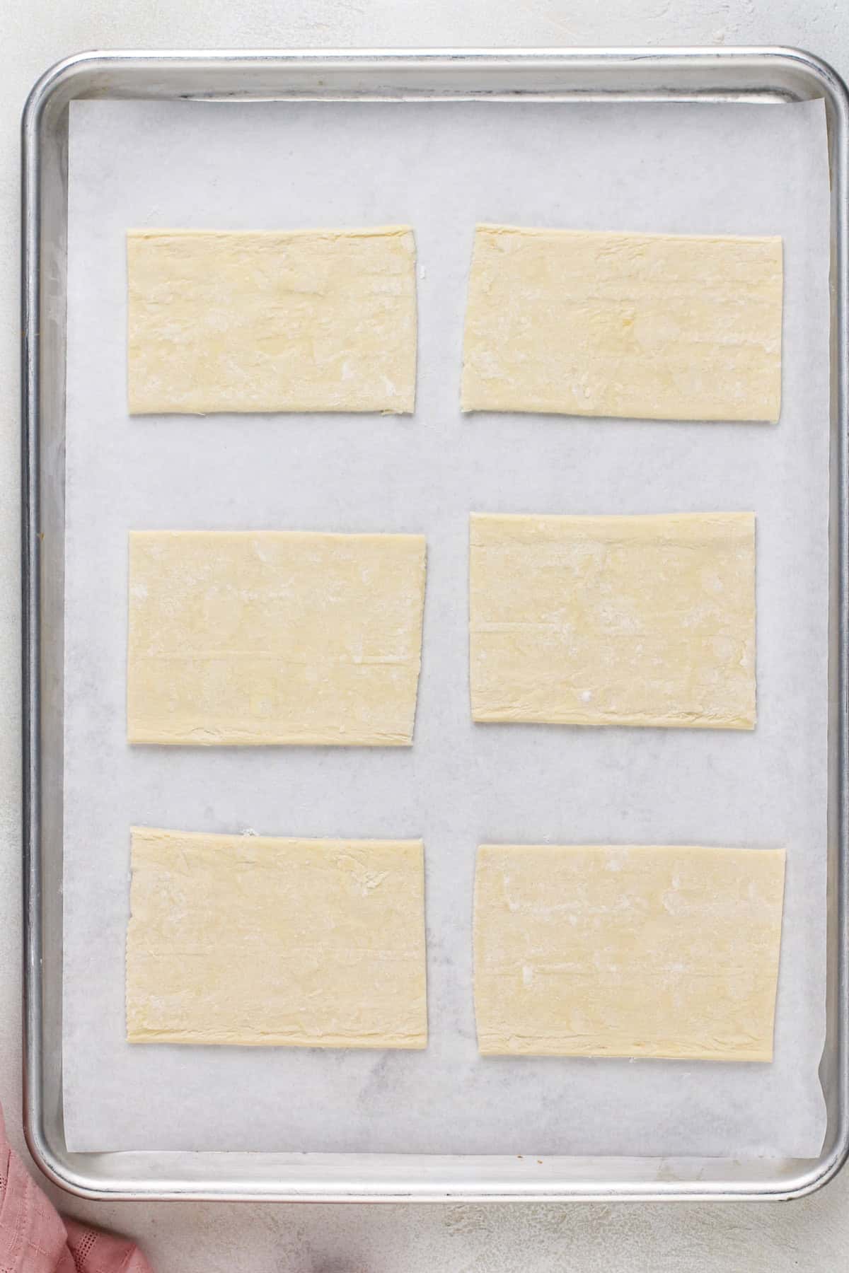 Six rectangles of puff pastry set on a parchment-lined baking sheet.