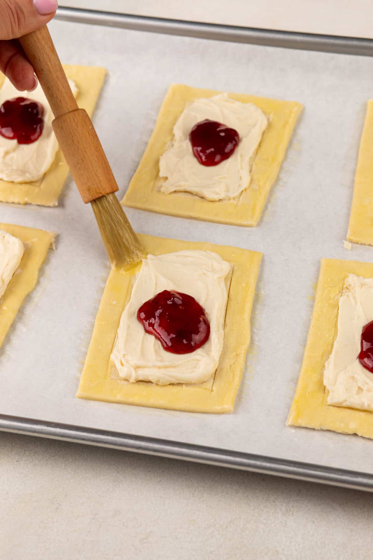 Pastry brush brushing egg wash on the edges of puff pastry danishes.