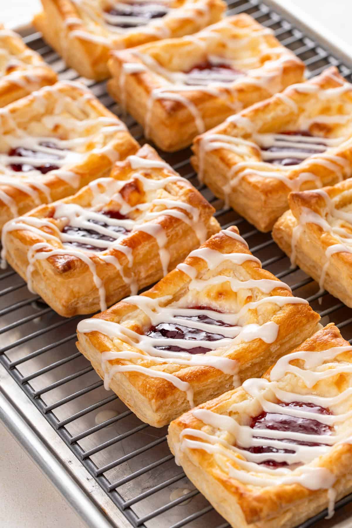 Glazed puff pastry danishes resting on a wire rack.