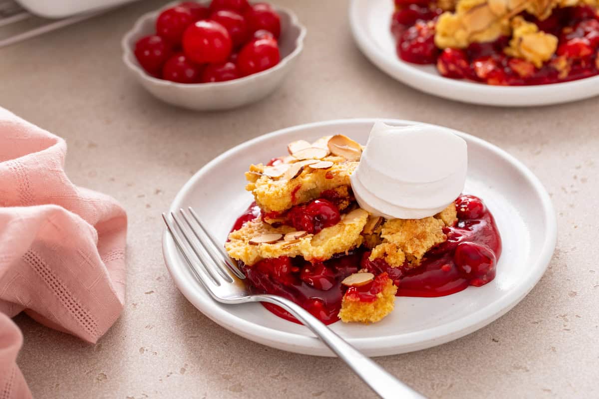 Serving of cherry dump cake next to a fork on a white plate.