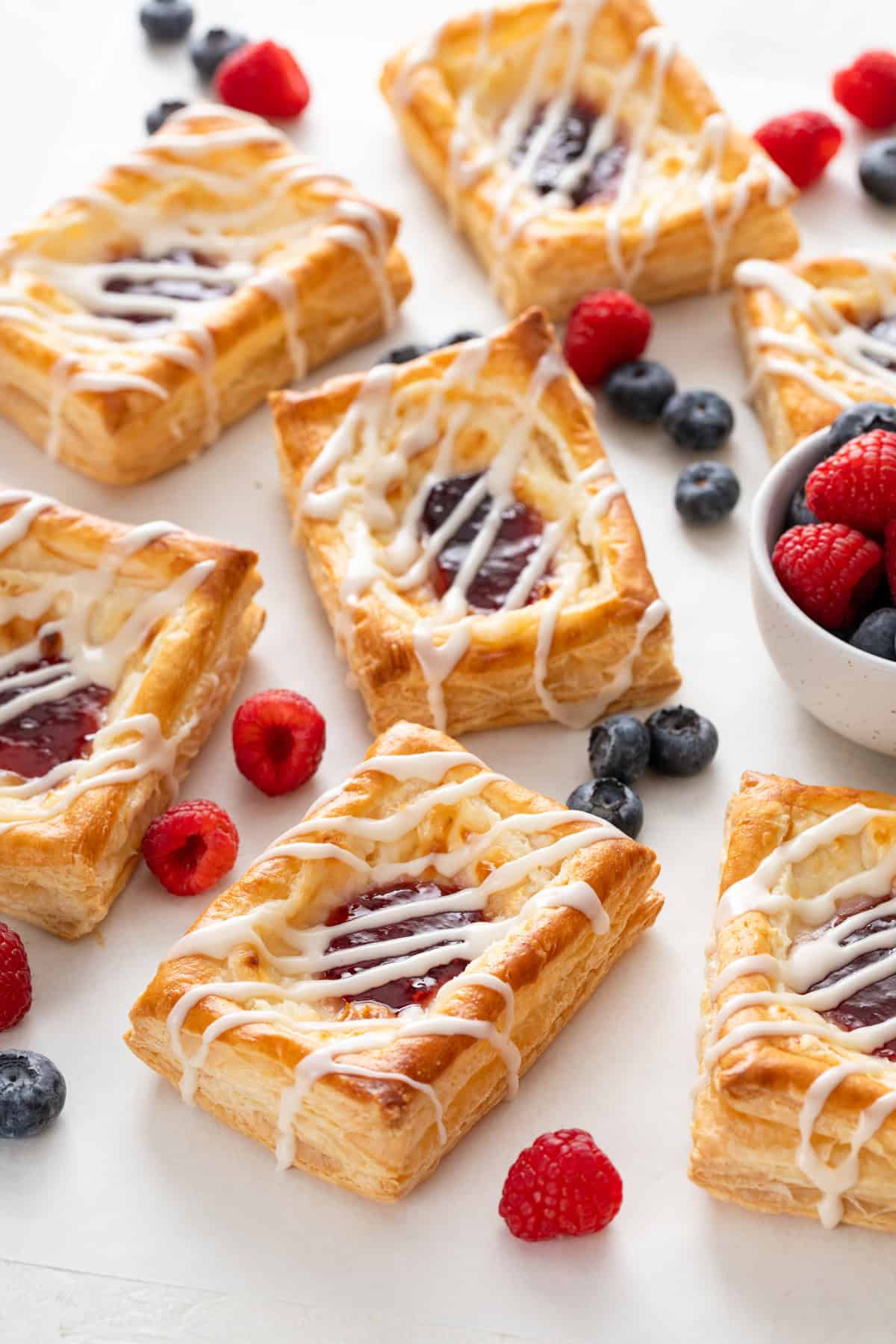 Puff pastry danishes scattered on a white countertop with mixed fresh berries.