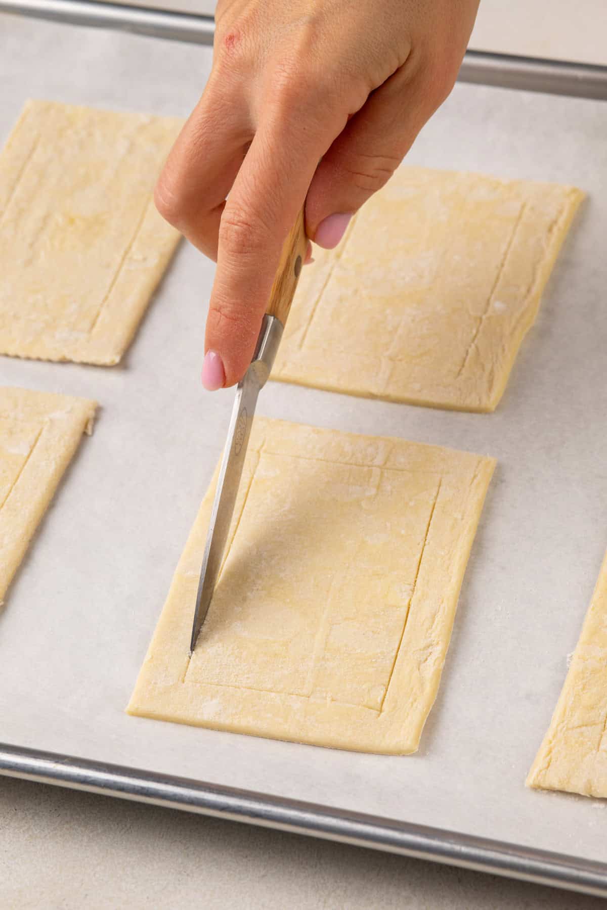 Hand using a knife to score rectangles of puff pastry.