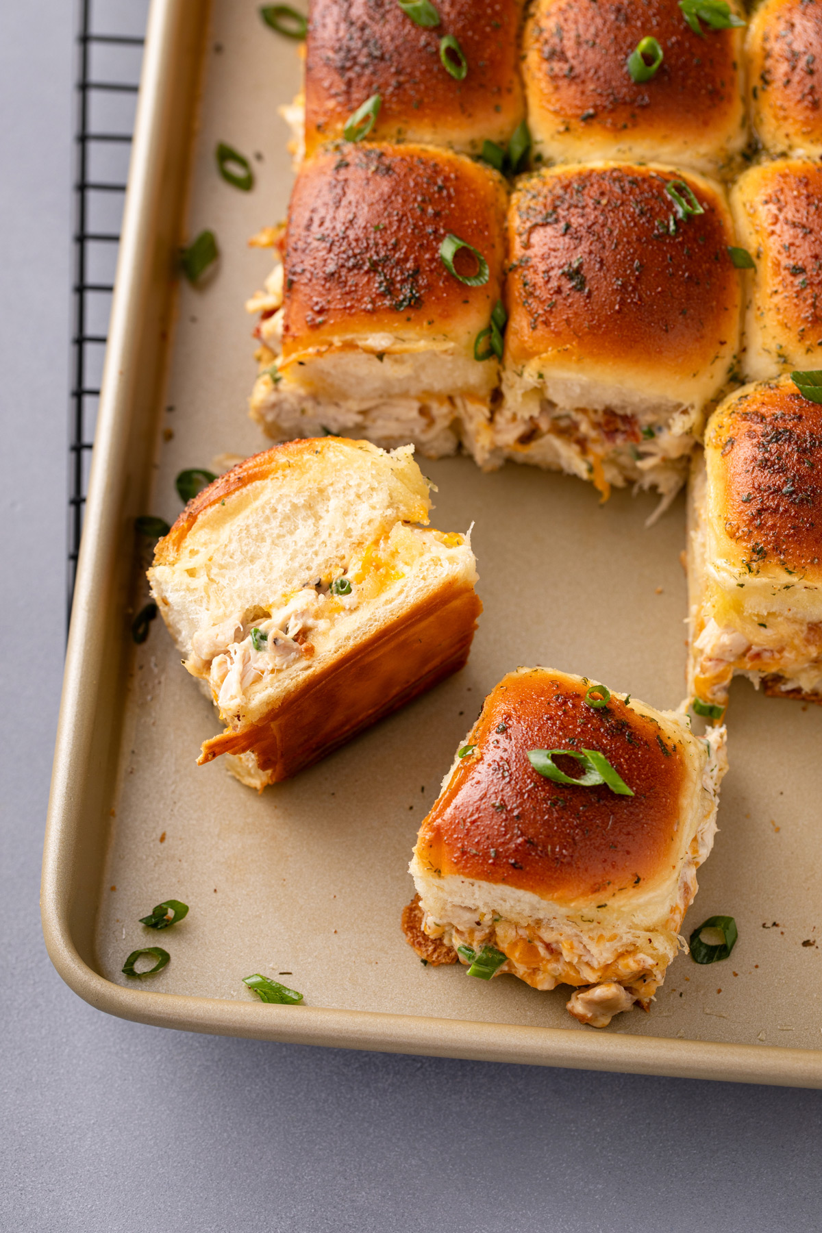 Two chicken bacon ranch sliders cut from the rest of the sliders on a baking sheet.