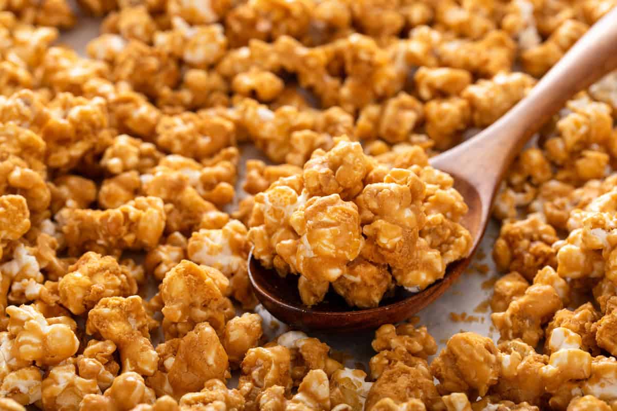 Wooden spoon scooping homemade caramel corn off of a baking sheet.