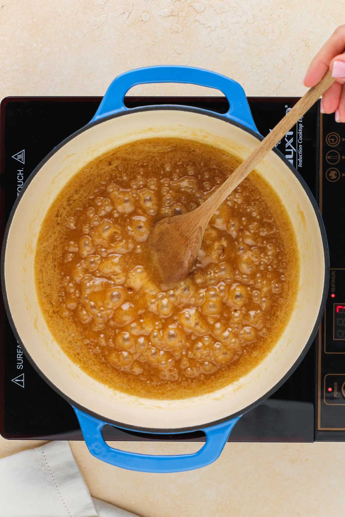 Wooden spoon stirring boiling caramel in a saucepan.