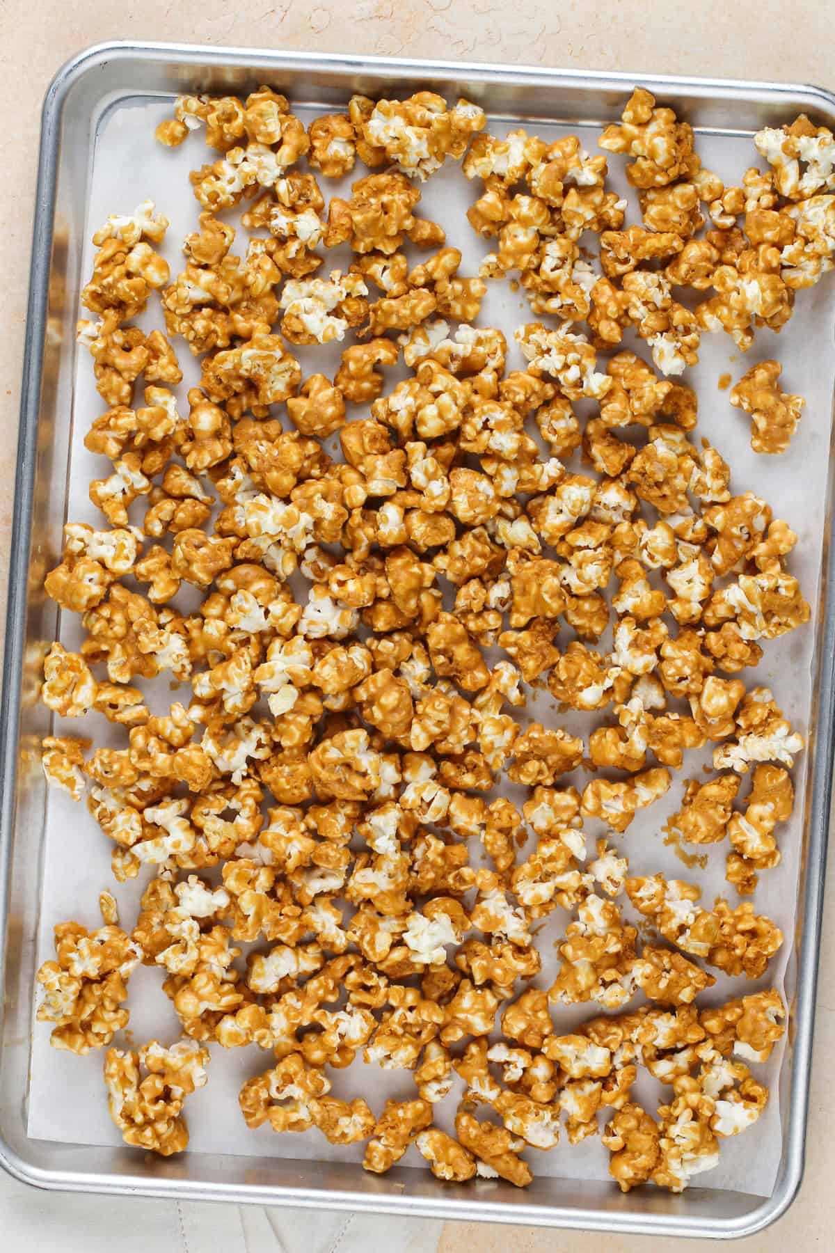 Unbaked caramel corn spread out onto a parchment-lined baking sheet.