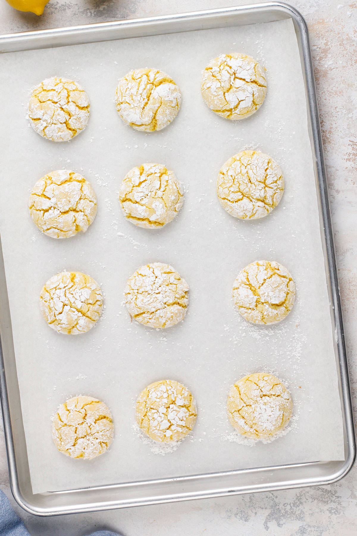 Baked lemon crinkle cookies on a parchment-lined baking sheet.