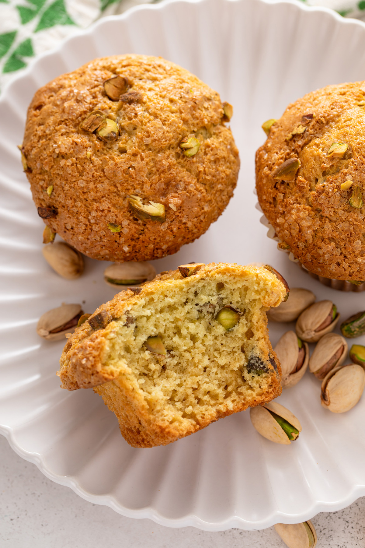 Three pistachio muffins on a white plate with a bite taken from one.