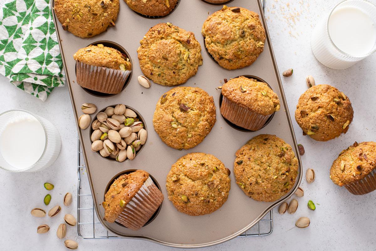 Overhead view of pistachio muffins and pistachio nuts in a muffin tin.