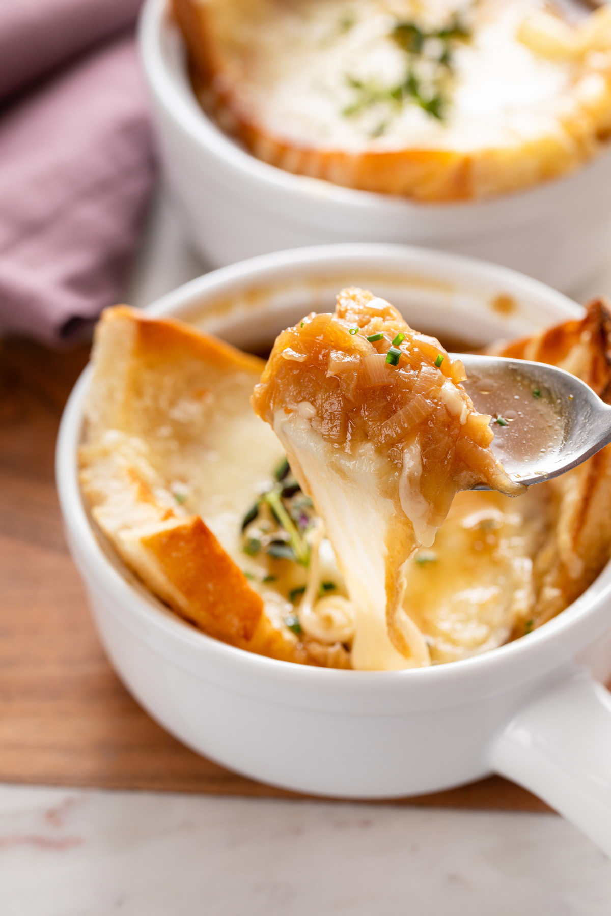 Spoon picking up a bite of french onion soup, showing the cheese pull as the spoon pulls away.