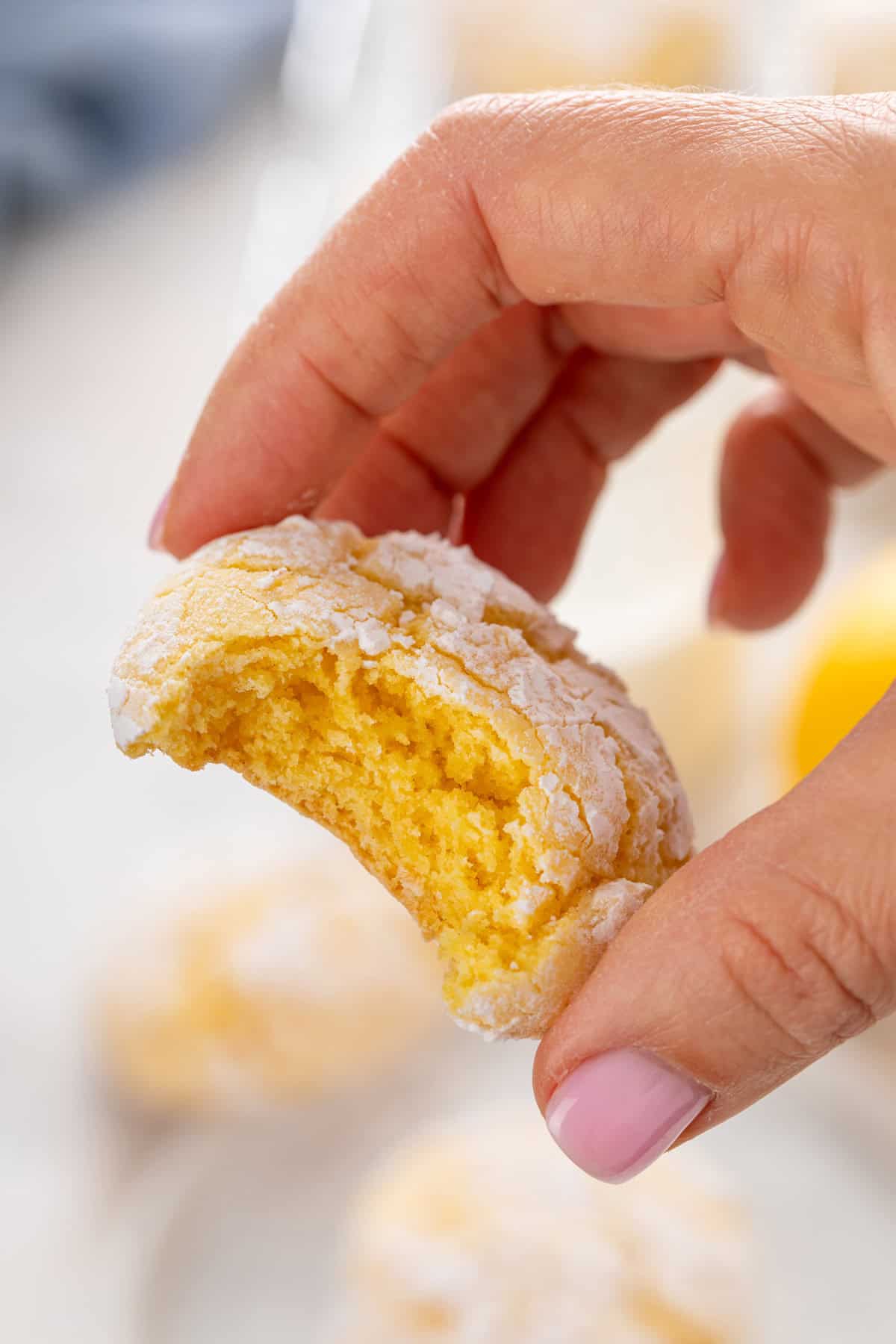 Hand holding up a lemon crinkle cookie with a bite taken from it.