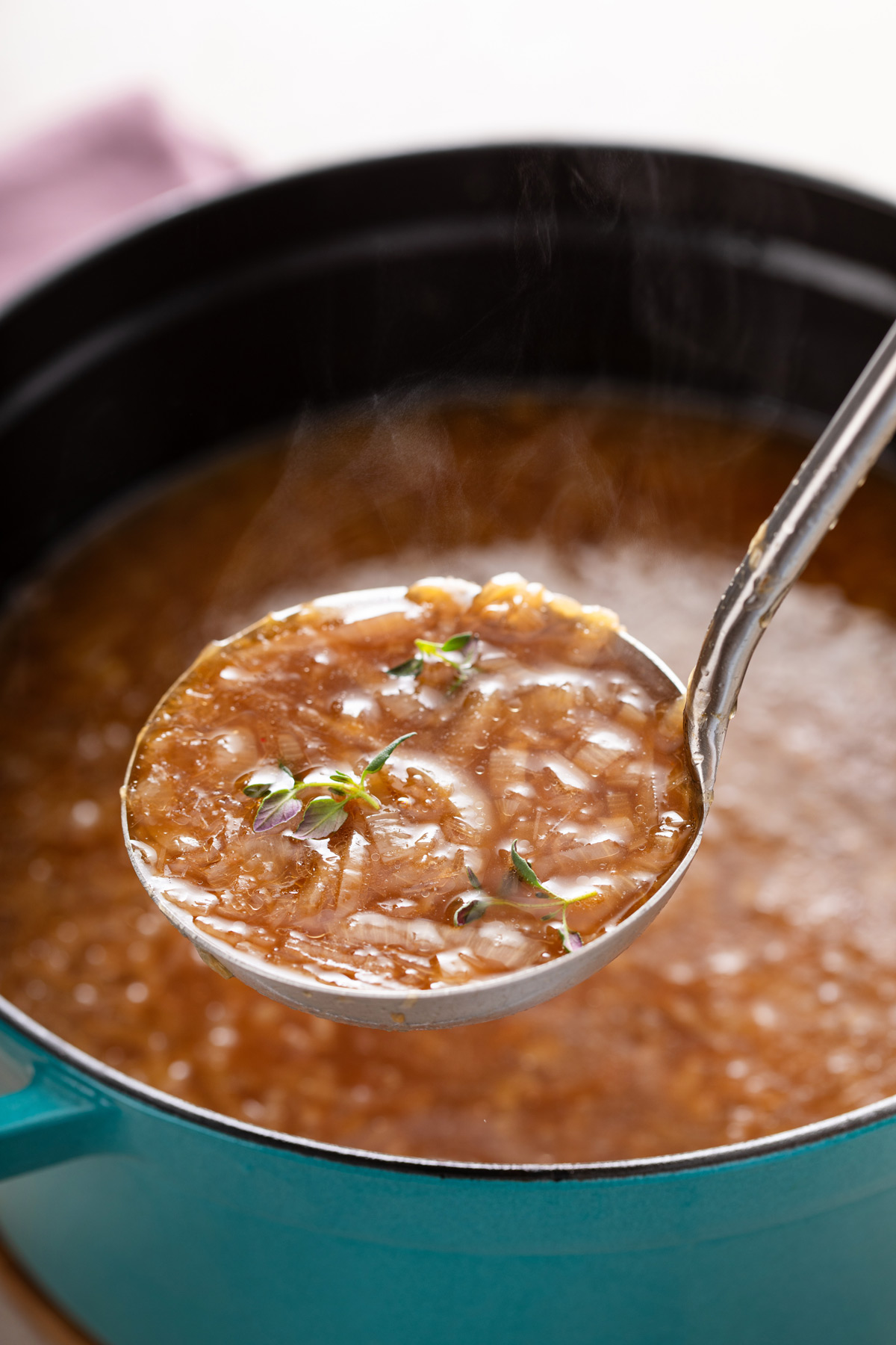 Ladle holding up french onion soup over a pot of the soup.