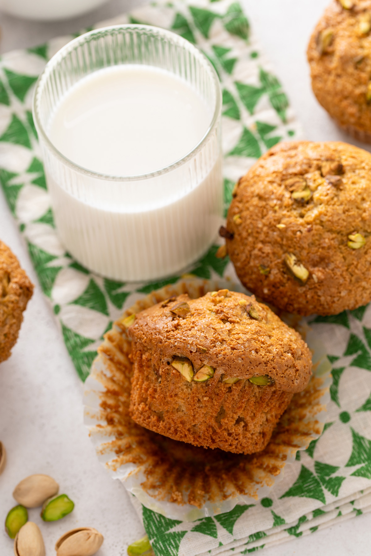 Two pistachio muffins next to a glass of milk on a green and white napkin.