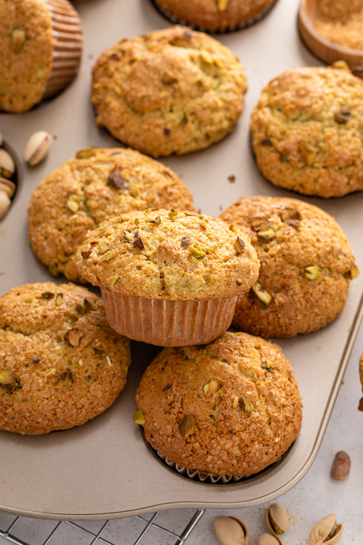 Baked pistachio muffins piled on top of a muffin tin.