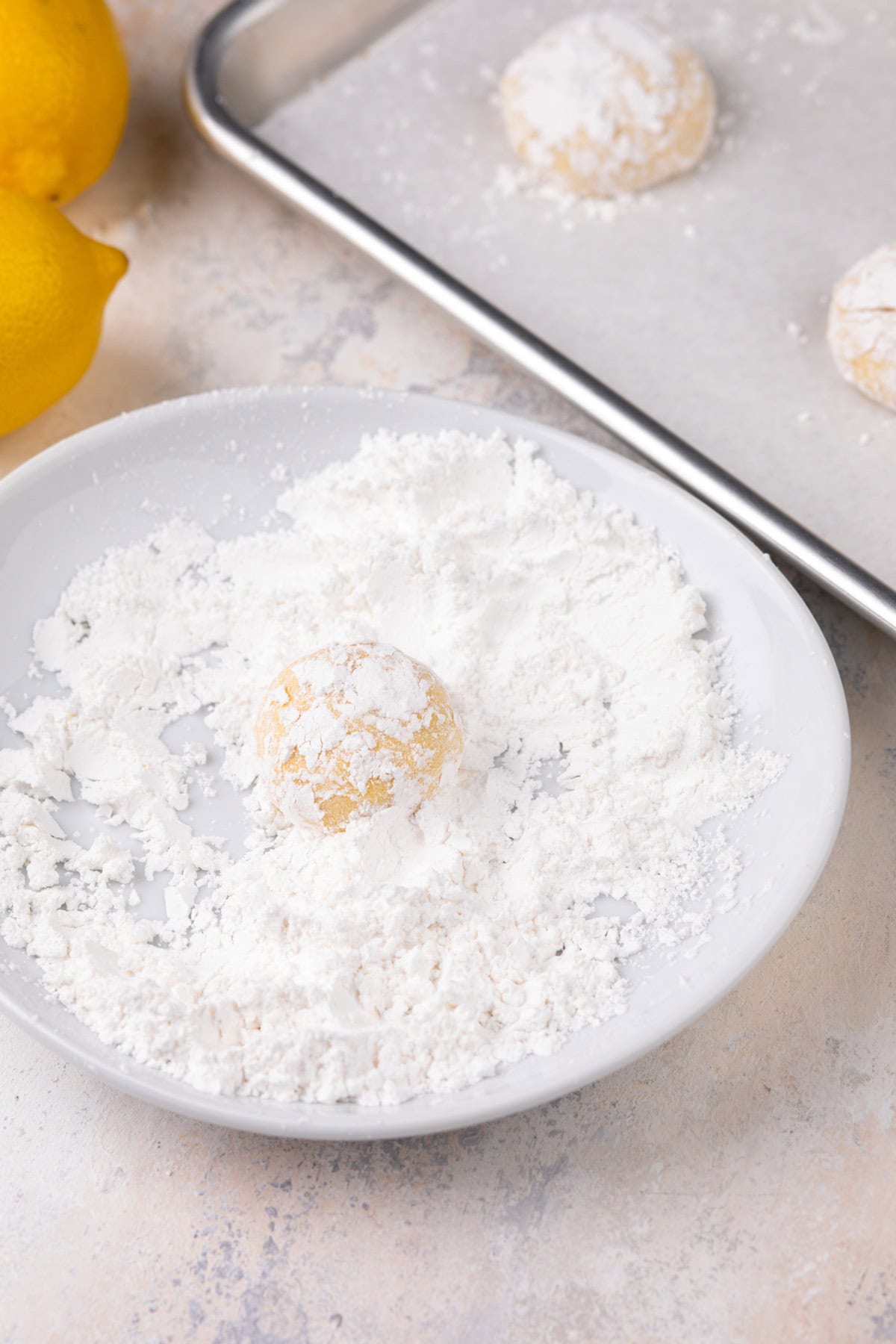 Rolled lemon crinkle cookie dough being rolled in powdered sugar.