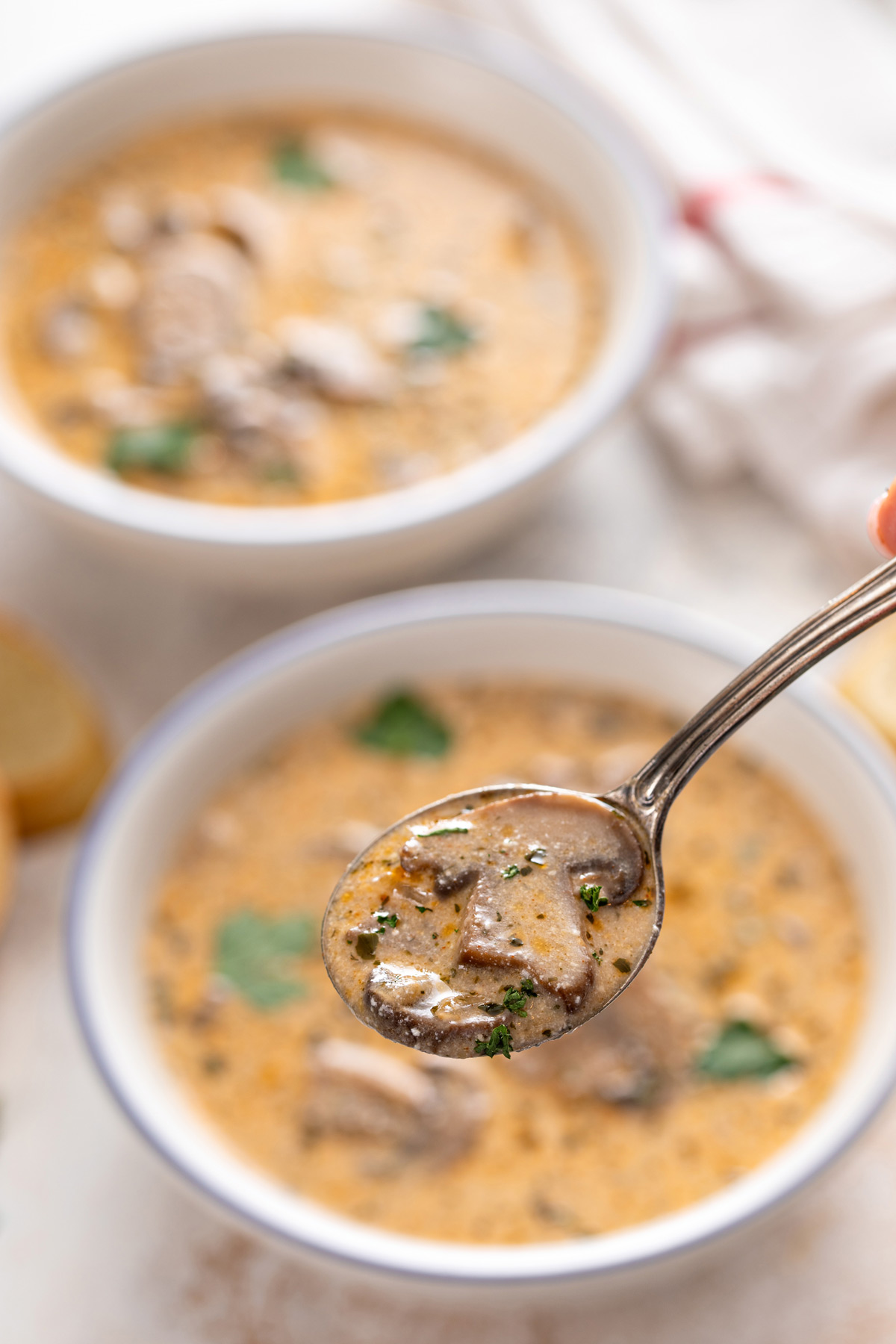 Spoon filled with creamy mushroom soup over a bowl.