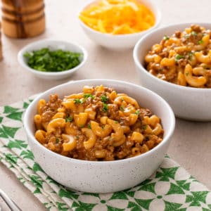 White bowl filled with homemade cheeseburger helper set on a green and white napkin.