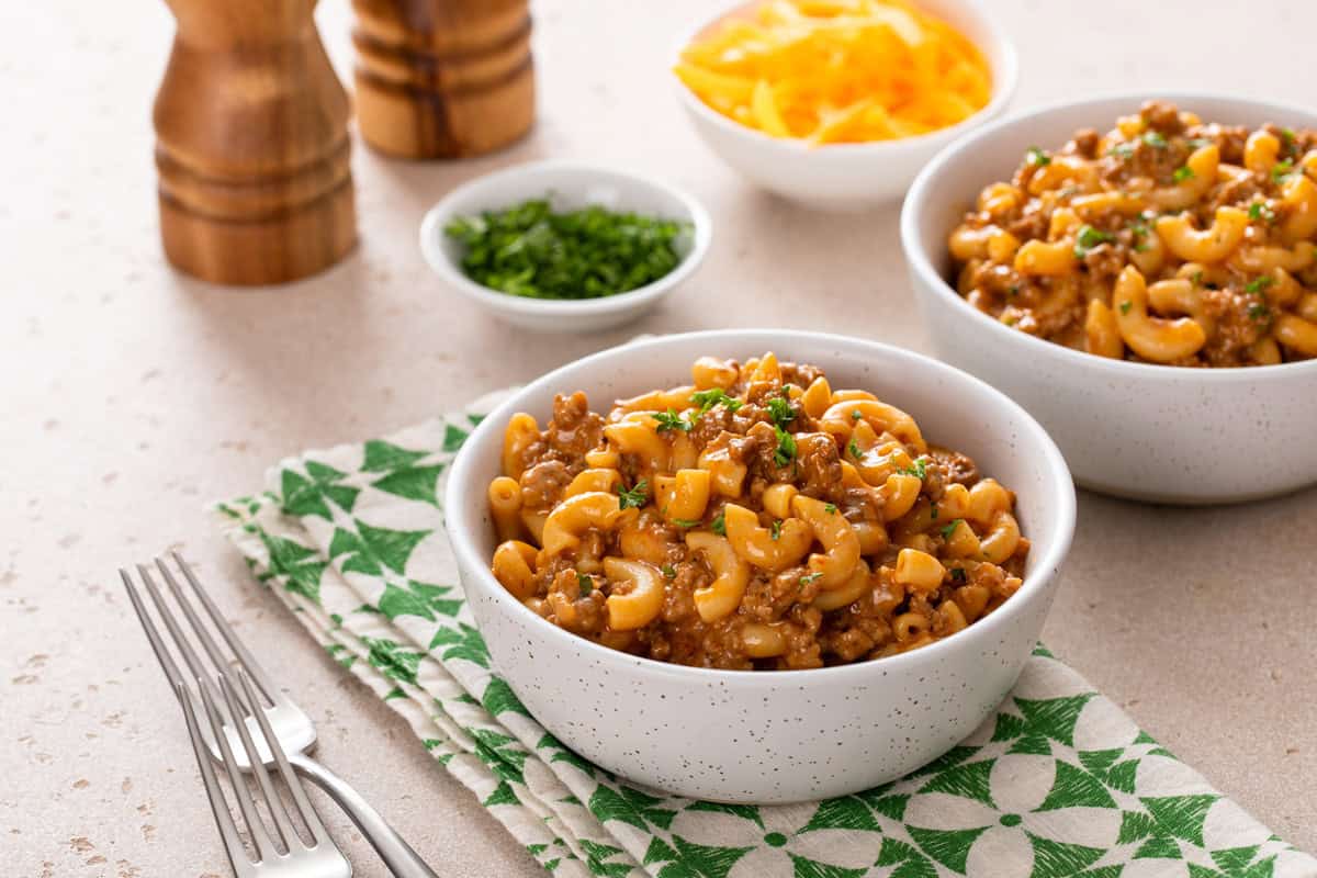 Cheeseburger helper in a white bowl set on a green and white napkin on a countertop.