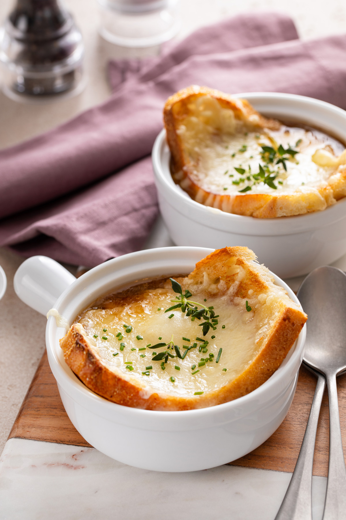 Two white bowls filled with french onion soup and topped with cheese toast.