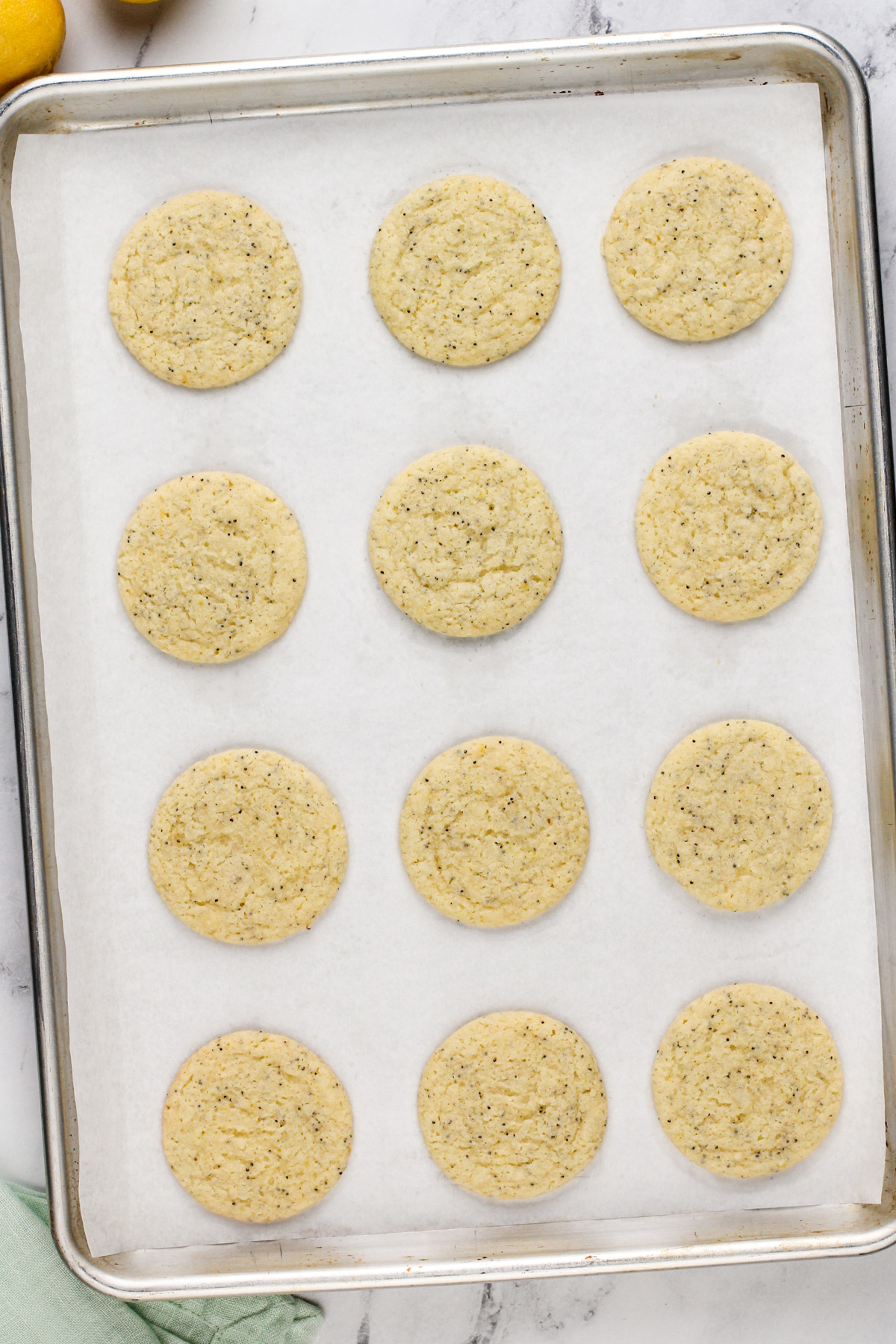 Baked lemon poppy seed cookies cooling on a parchment-lined baking sheet.