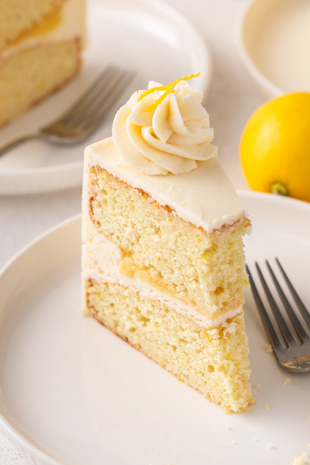 bite taken from a slice of lemon layer cake on a white plate.