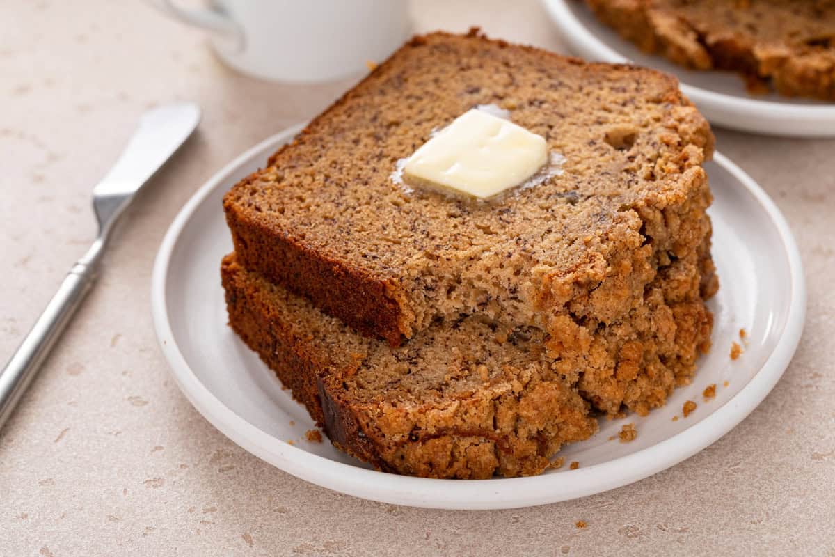 Bite taken from a buttered slice of sour cream banana bread on a white plate.