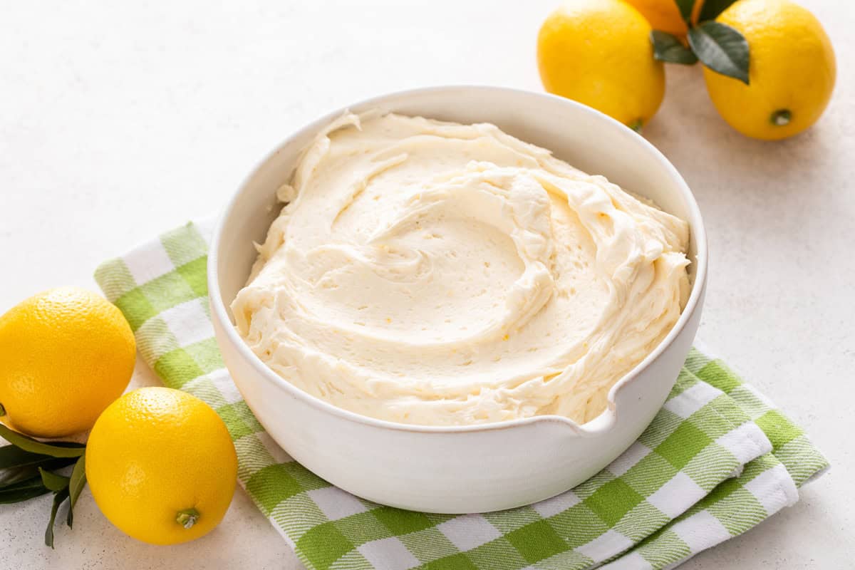 Lemon buttercream in a white bowl set on a green and white napkin.