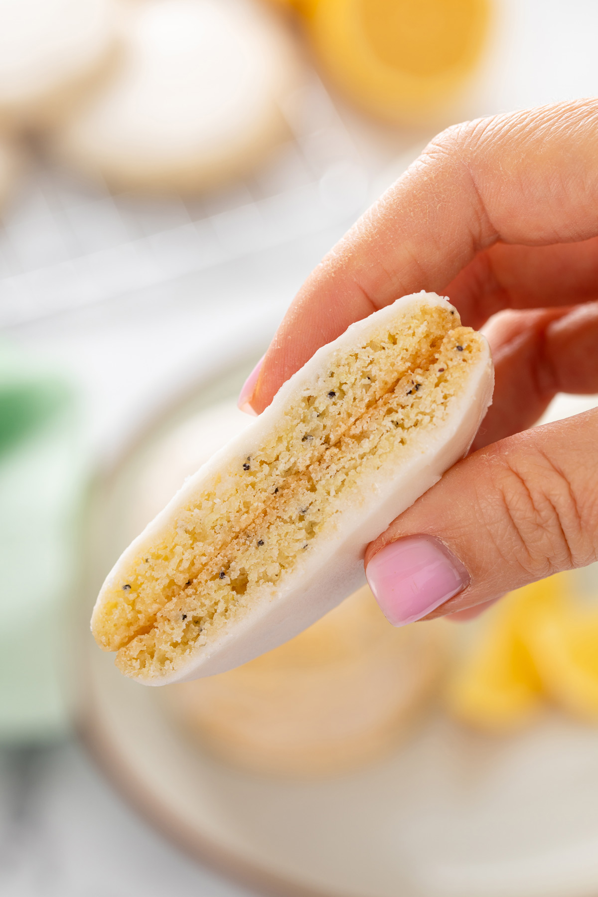 Hand holding up a halved lemon poppy seed cookie to show the inside texture.