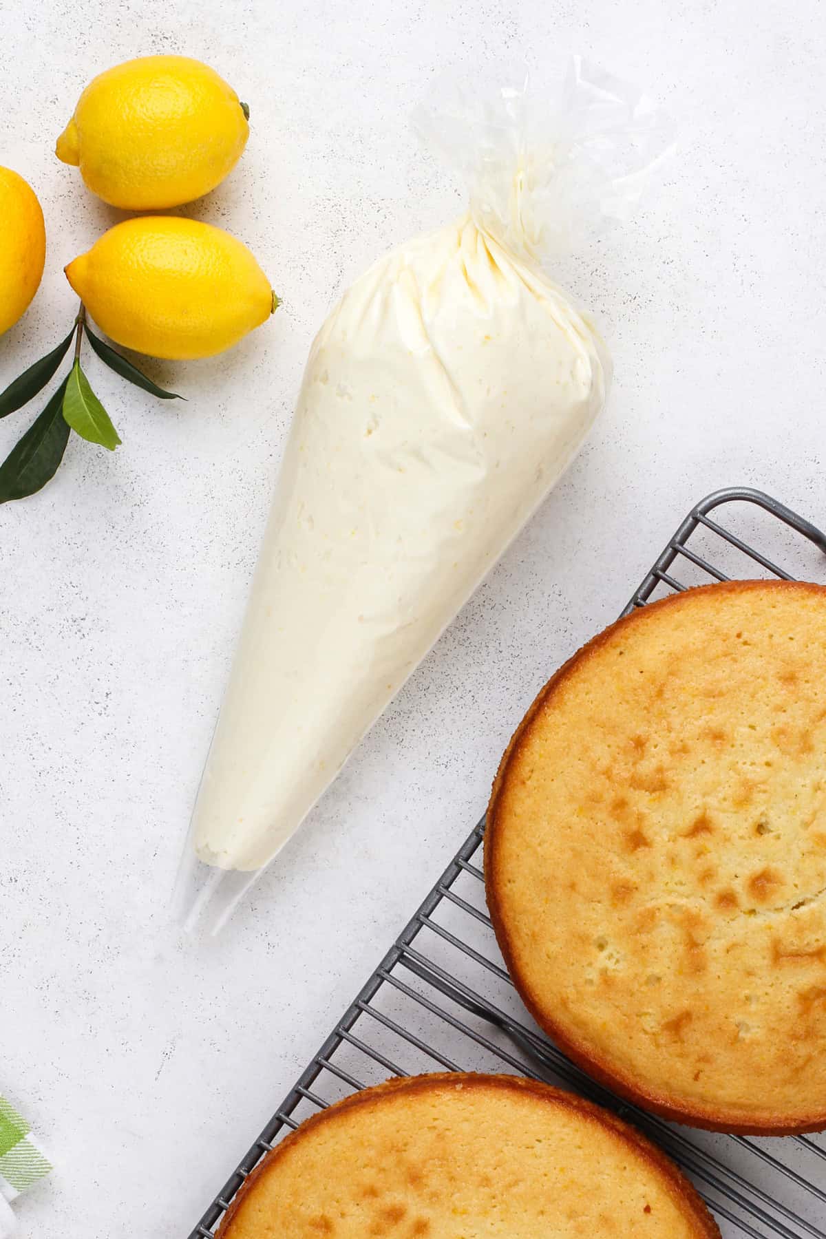 Piping bag filled with lemon buttercream frosting next to cake layers on a wire rack.