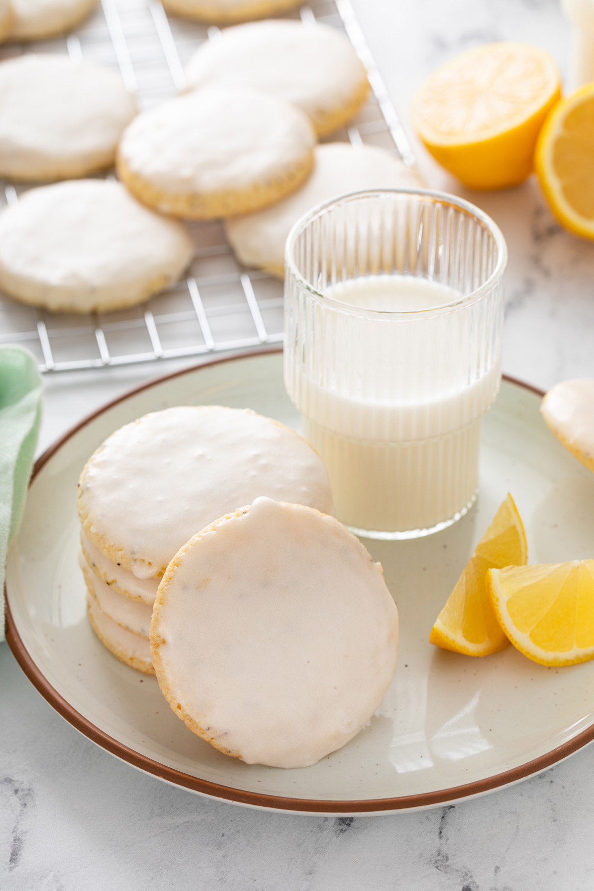 Stack of lemon poppy seed cookies with another cookie leaning against it in front of a glass of milk.