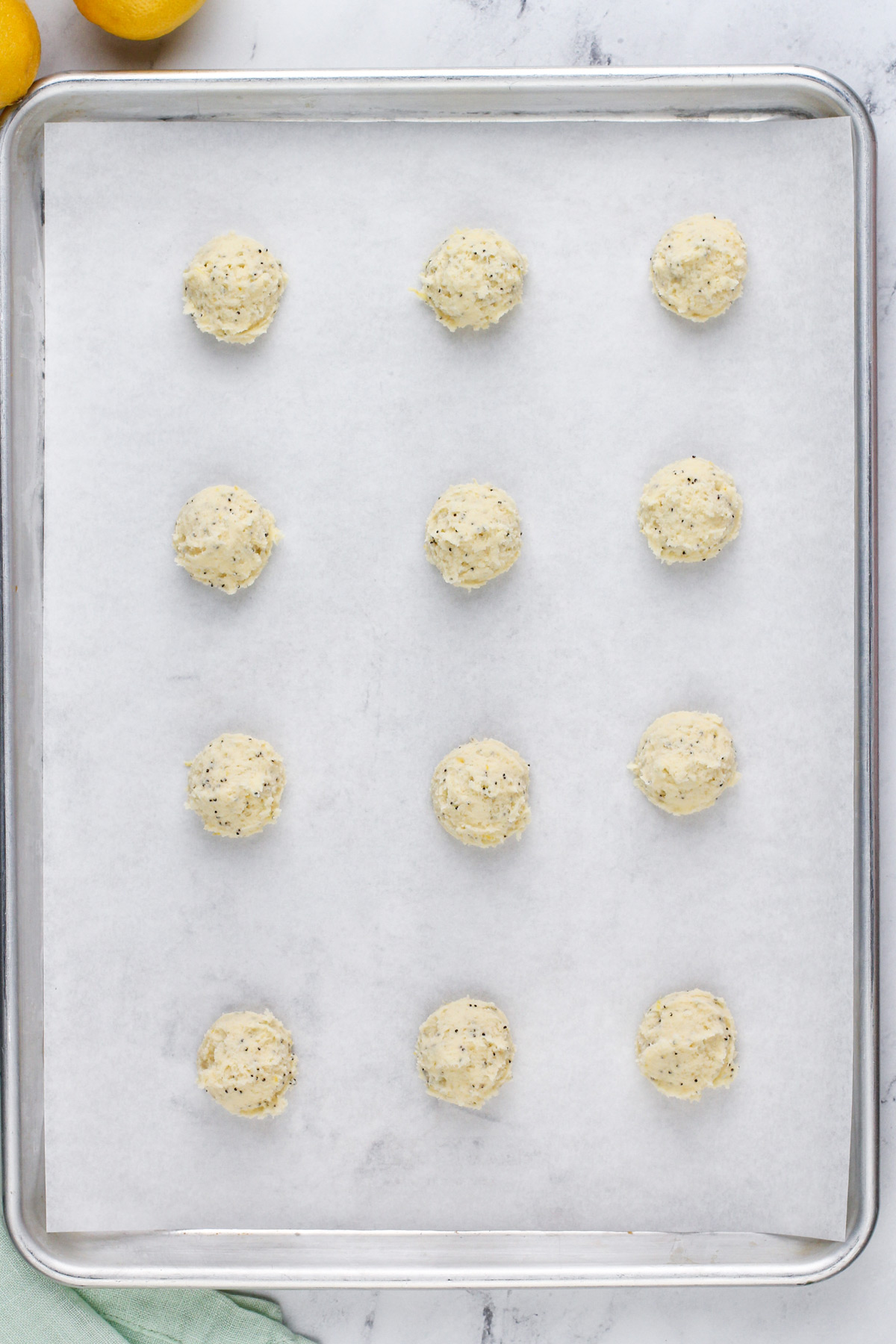 Unbaked lemon poppy seed cookies on a parchment-lined baking sheet, ready to go in the oven.