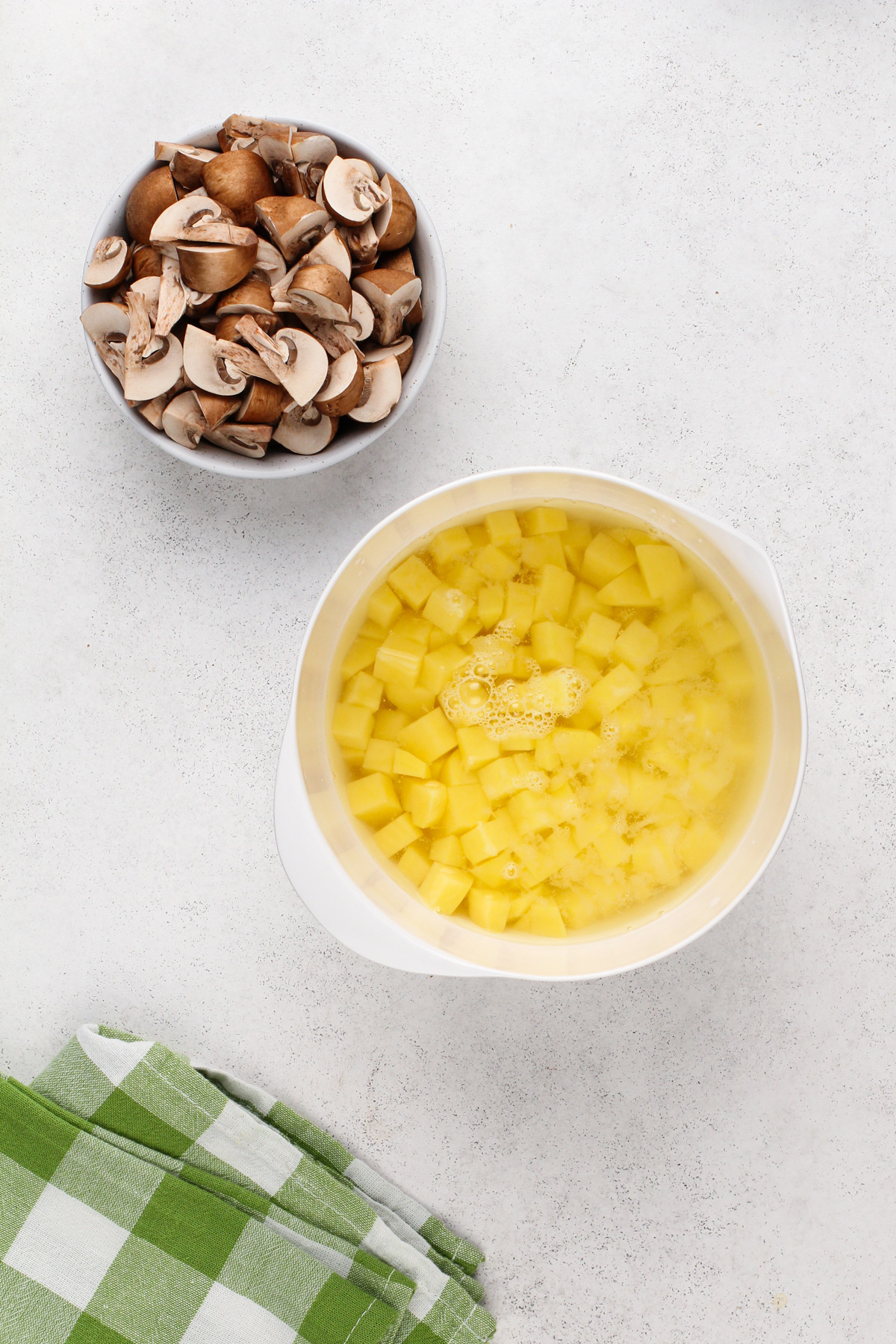 Diced potatoes in a bowl of water next to a bowl of cut mushrooms.