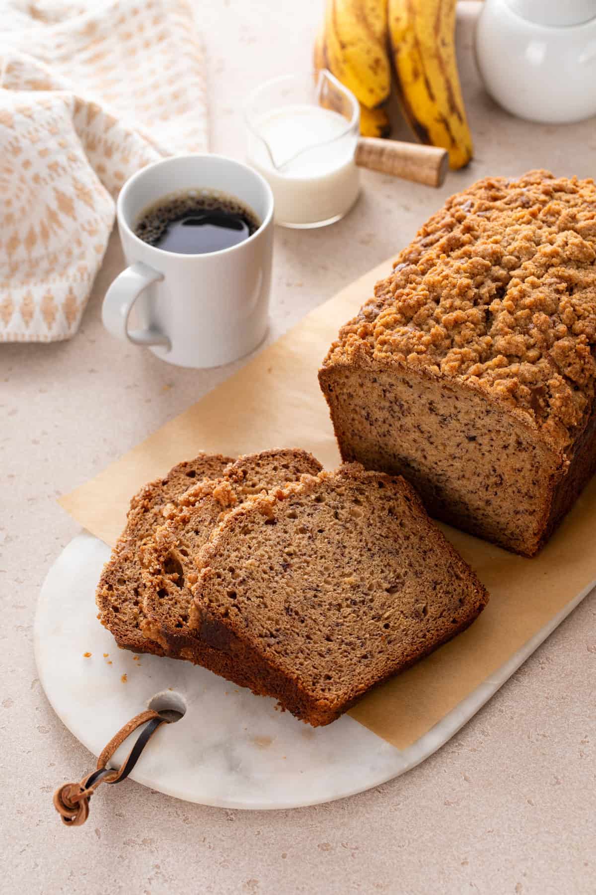 Sliced loaf of sour cream banana bread on a marble board next to a cup of coffee.